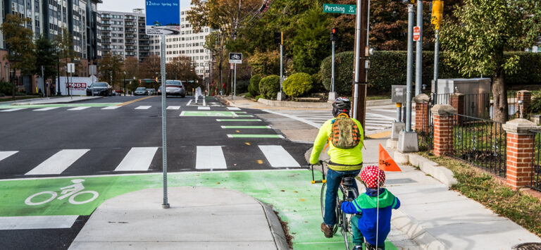 A father and son ride a bicycle on a protected bike lane.