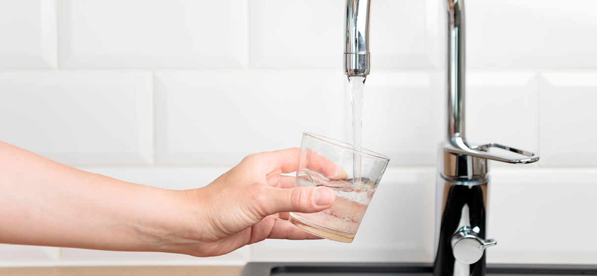 A person fills a cup of drinking water from the sink.