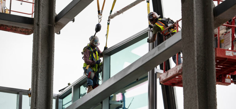 Construction workers install glass panels to a building frame for an airport terminal under construction.