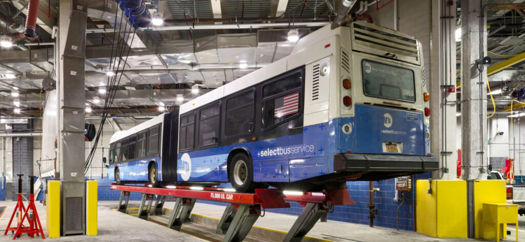 An NYC Transit bus on a service bay inside a bus depot.