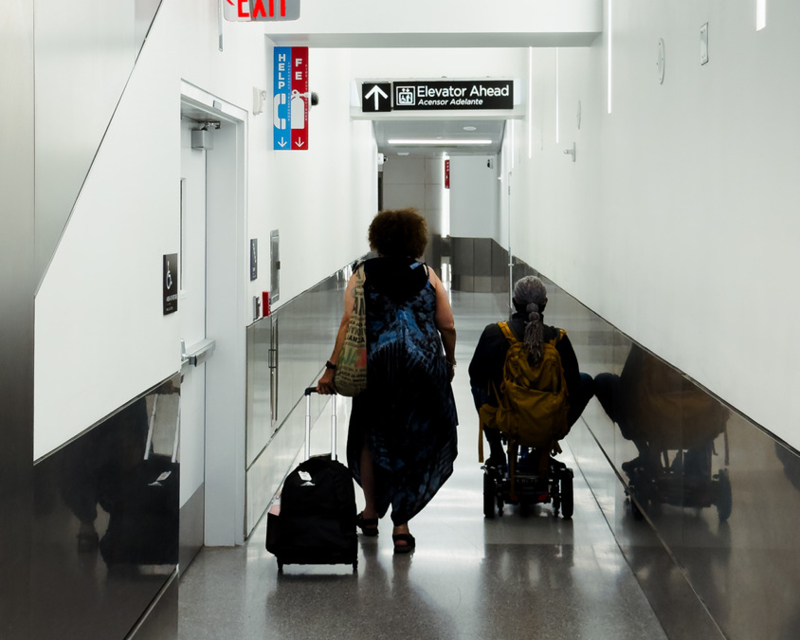 A passenger in a wheelchair and their companion heading towards the elevators.