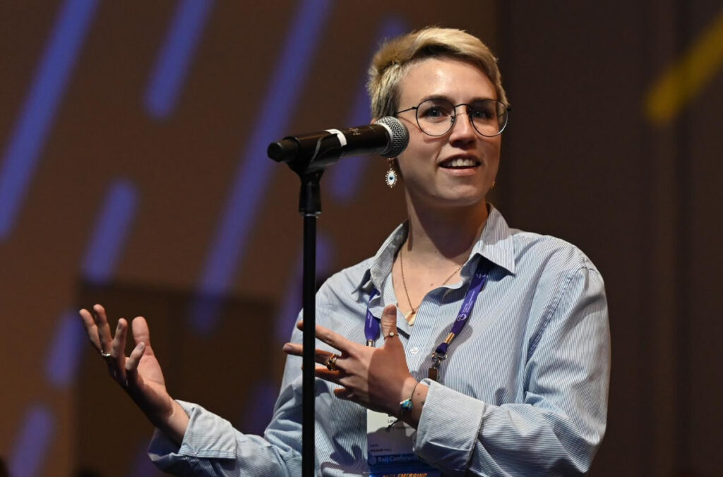 STV's Lauren Garoppo presenting on stage in front of a microphone at the APTA Mobility conference.