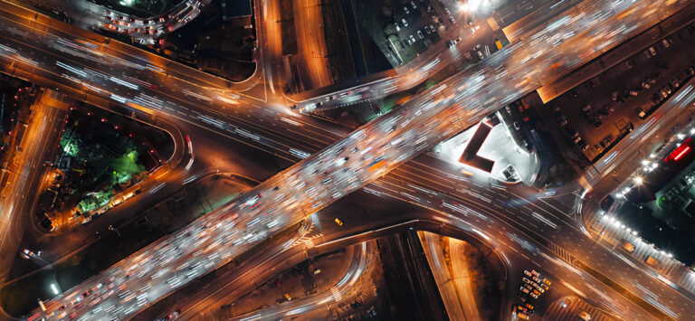 Birds-eye view cars speeding along a highway intersection at night.