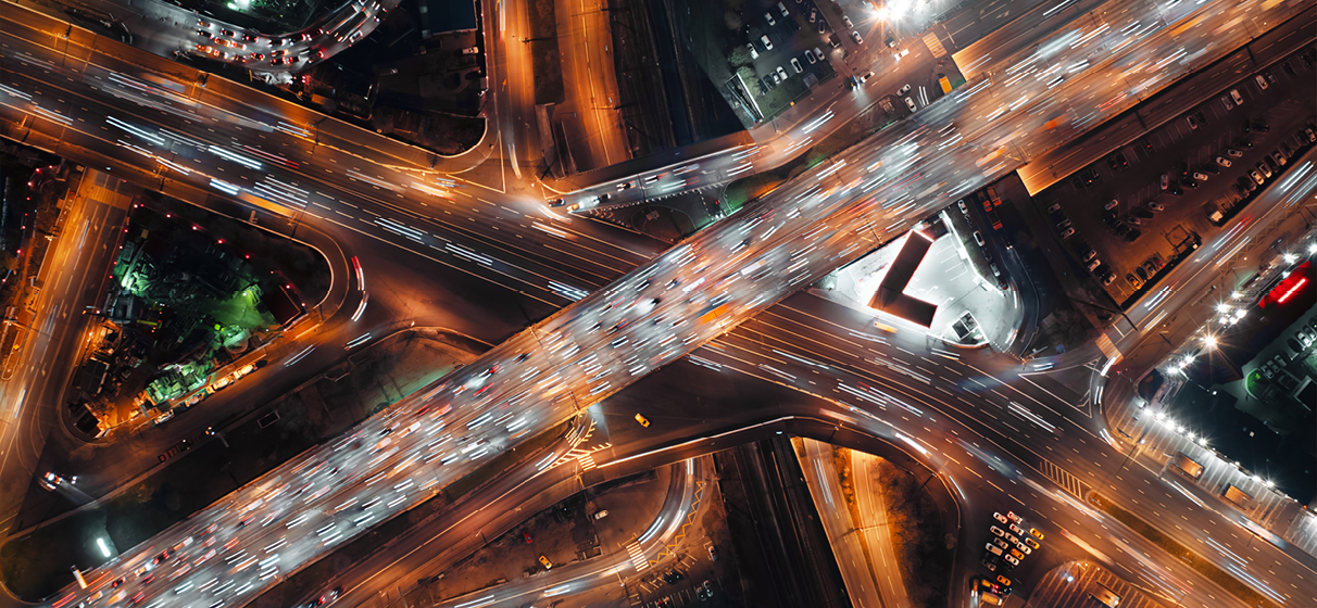 Birds-eye view cars speeding along a highway intersection at night.