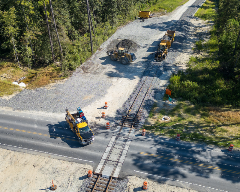 Aerial view of construction vehicles working at intersection of rail tracks and roadway.