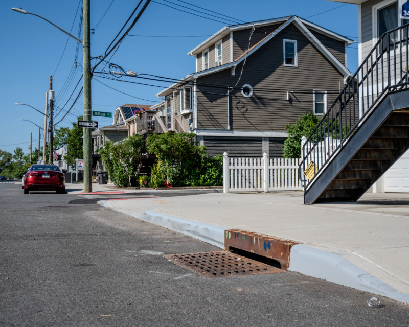 Close-up of storm sewer on Staten Island roadway in front of houses.
