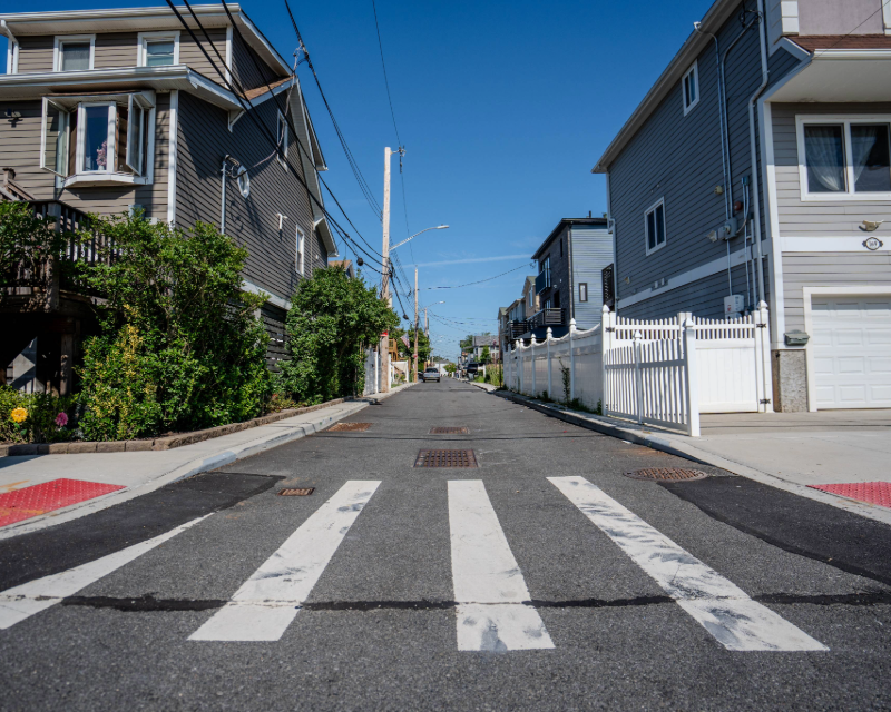 Close up of crosswalk and ADA ramps with storm sewers behind along Staten Island neighborhood street.