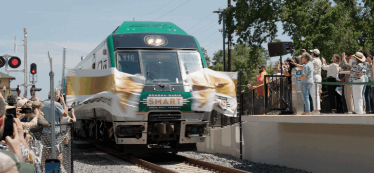 A SMART train breaking through a grand opening sign at the opening ceremony for the SMART Windsor Extension in California.