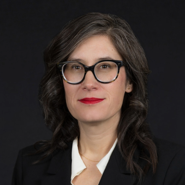 Headshot of woman with dark hair, dark background and glasses