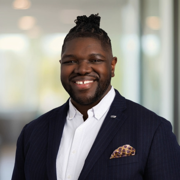 Headshot of man in black suit and white shirt with office background