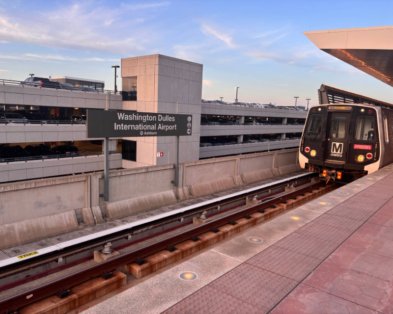 Train arriving at Washington Dulles International Airport WMATA station with parking structure in background.