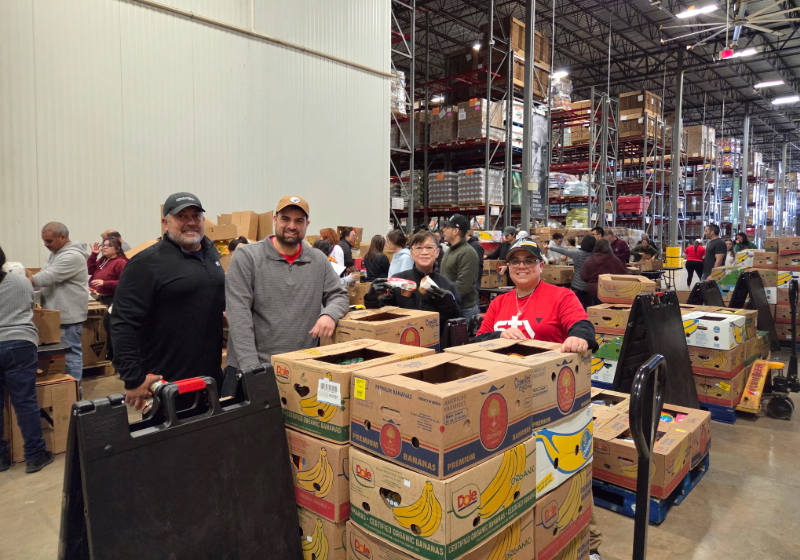 STV volunteers pose behind boxes of food at San Antonio food bank.