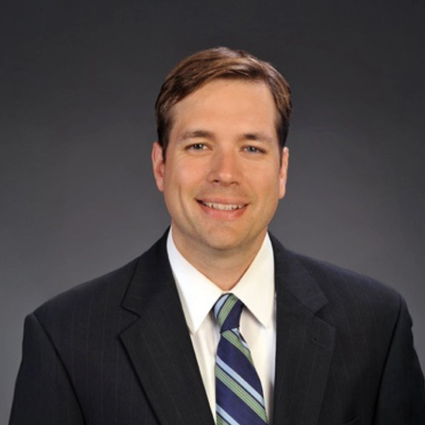 Headshot of man in black suit with grey background