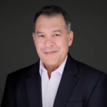 Professional headshot of man in white shirt with black suit against gray background.