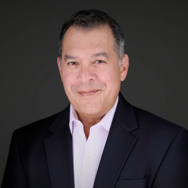 Professional headshot of man in white shirt with black suit against gray background.
