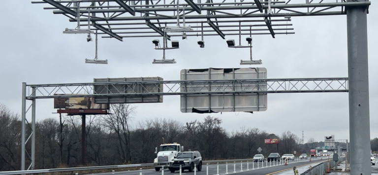 Cars and trucks on highway toll road on overcast day with tolling equipment overhead