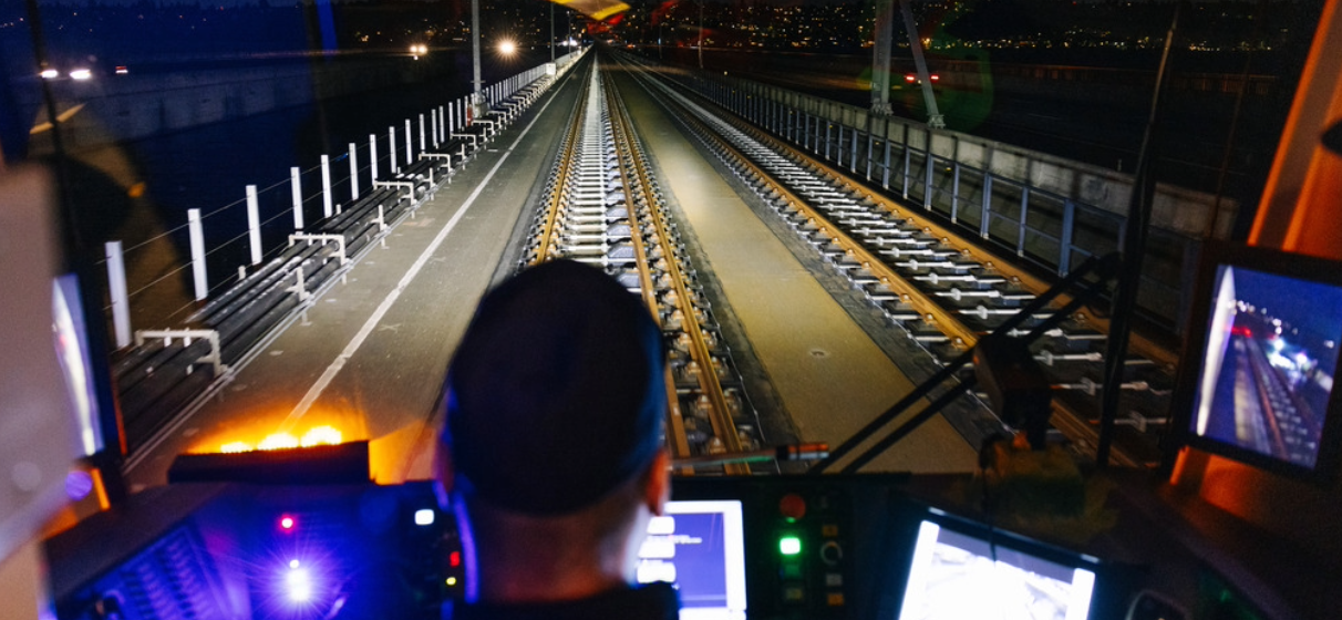 View from behind a train operator at night as he drives down a railroad