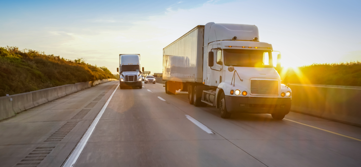 Two freight trucks traveling down a roadway.