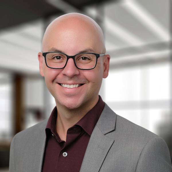 Headshot of man with glasses in grey blazer and dark red top