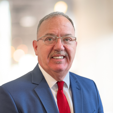 headshot of man in glasses with blue suit and red tie