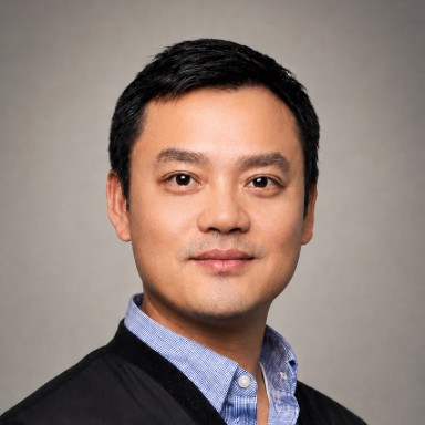 headshot of man in blue dress shirt and black blazer with black hair