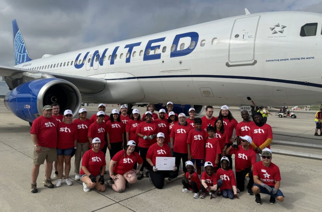 STV team in STV red t-shirts pose in front of United Airlines jet on the tarmac at Dulles Airport.