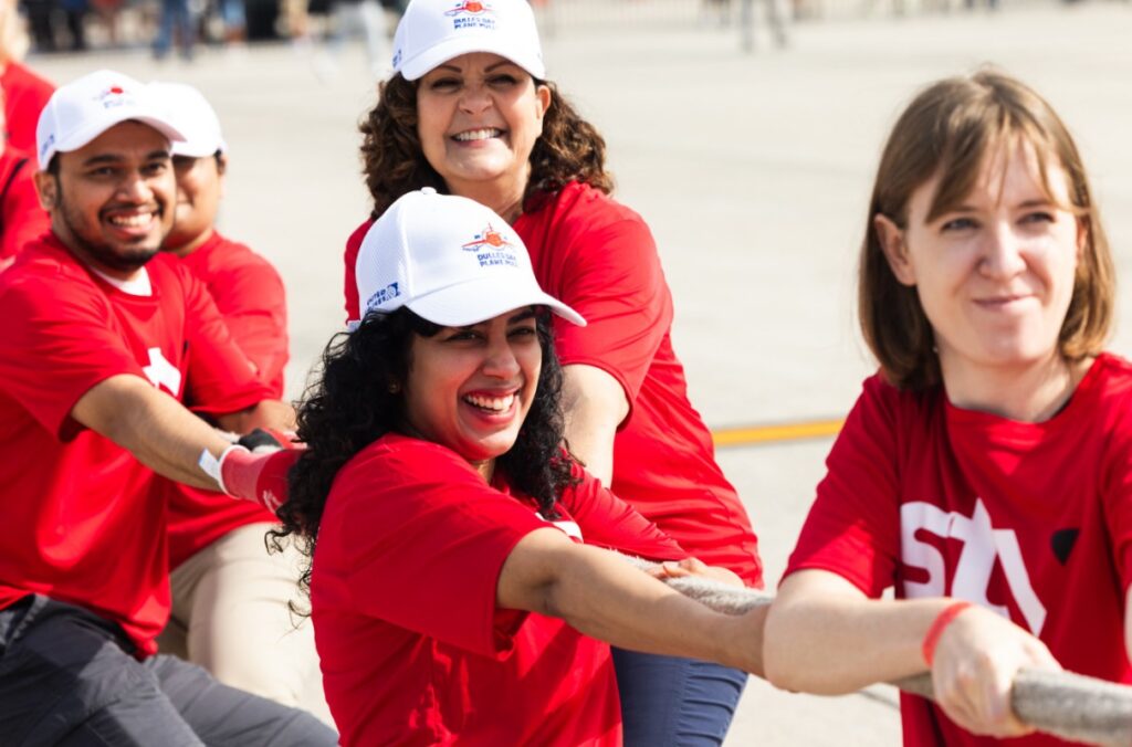 Close up of STV team members, smiling, as the pull a rope on the tarmac at Dulles Airport.